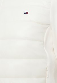 Λευκό αμάνικο μπουφάν με επένδυση και υφή καπιτονέ, πλευρικό φερμουάρ και κεντημένο λογότυπο σε μπλε, κόκκινο και λευκό. Μαλακό ύφασμα με λεία υφή.