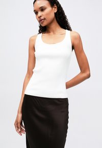 Top a righe bianco con scollatura a cuore, abbinato a una gonna liscia in satin marrone scuro, che mette in evidenza il contrasto tra trame e colori.