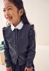 Cardigan grigio con spalle arricciate, bottoni sul davanti e camicia bianca con colletto sotto. Tessuto morbido, vestibilità casual, ideale per essere indossato a strati.