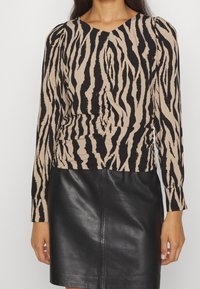 Haut à manches longues beige avec des rayures zèbre noires, doté d'un col en V et de détails froncés à la taille. Associé à une jupe en cuir noir.