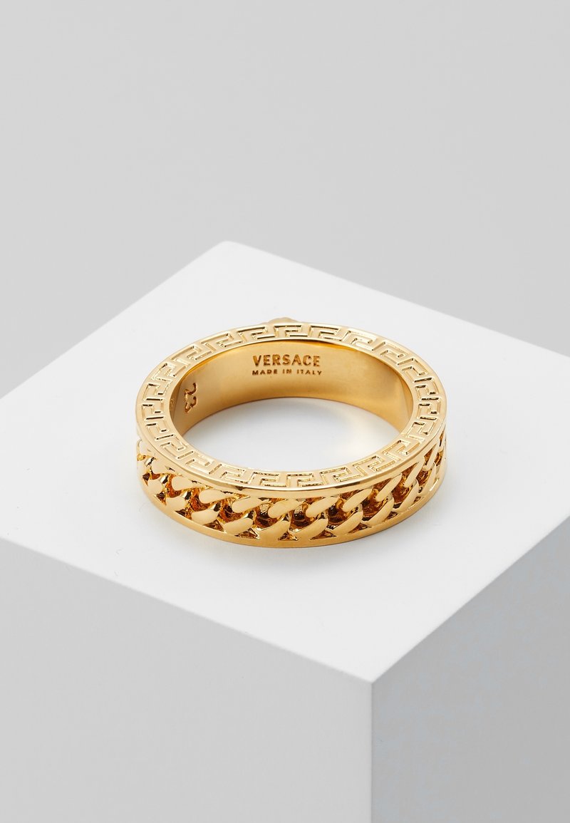 Bague Versace en or avec motif clé grecque et design chaîne sur l’anneau, gravée avec "VERSACE MADE IN ITALY" à l’intérieur.