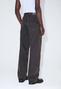 Musta rento istuvuinen farkkuhousu, jossa on kaksi takataskua, näkyvät ompeleet ja kevyt haalistuma. Yhdistetty valkoiseen toppiin.