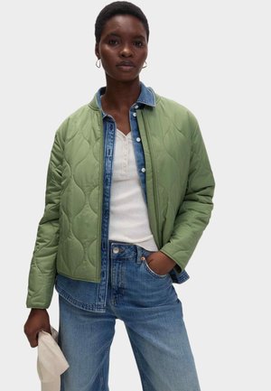 Pikowana zielona kurtka z dżinsowym kołnierzem, noszona na białej bluzce, w połączeniu z jasnoniebieskimi spodniami o szerokich nogawkach. Modelka trzyma beżową czapkę.