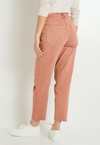 Un pantalon en denim rose clair avec une taille haute, des jambes fuselées et deux poches arrière, associé à des baskets blanches.
