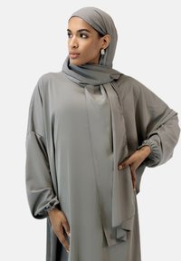 Robe gris clair à manches longues et poignets froncés, accompagnée d'un hijab assorti. Tissu lisse et fluide avec un léger éclat, sans motifs.