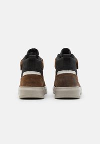 Hochsommer-Sneaker aus braunem Wildleder und schwarzem Stoff, mit einer beigen Gummisohle und verstellbaren Riemen an den Seiten.