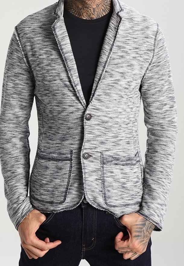 Blazer de punto jaspeado gris y negro con un corte entallado, cuello muesca y dos bolsillos frontales. Presenta dos botones y detalles de costura visibles.