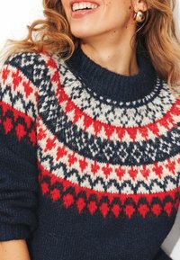 Pull en maille bleu marine avec col rond, présentant un motif multicolore en rouge, blanc et couleurs foncées. Texture douce avec des poignets côtelés.