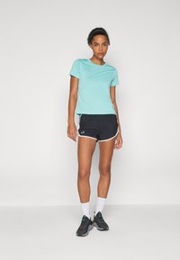 Lichtblauw, nauwsluitend T-shirt met korte mouwen, gecombineerd met zwarte sportshorts met witte bies, en zwarte sportschoenen.