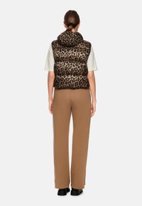 Padded vest with leopard print, featuring a hood, paired with light beige top and fitted brown pants with side slits, worn with black boots.