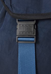 Námornícka taška z textílie s čiernou prackou loga Tommy Jeans. Pridaný textúrovaný modrý popruh, ktorý zdôrazňuje kompaktný dizajn.