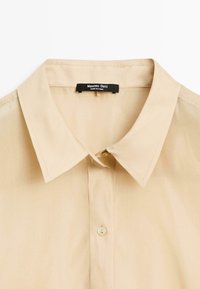 Beige overhemd met kraag van een gladde textuur, met een enkele knopsluiting bij de nek en een label met "Massimo Dutti."