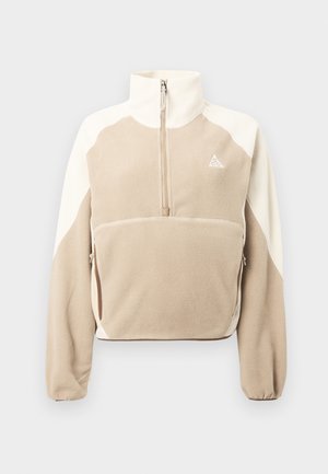 Pullover in pile beige e crema con zip e colletto alto, dotato di una tasca frontale e di un logo triangolare sul petto. Texture morbida.