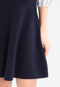 Robe skater bleu marine en tissu texturé, avec un corsage ajusté et une jupe évasée. La manche présente un motif rayé.