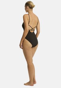 Maillot de bain noir avec des bretelles croisées au dos, design décolleté, texture lisse et détails dorés minimalistes à la hanche.