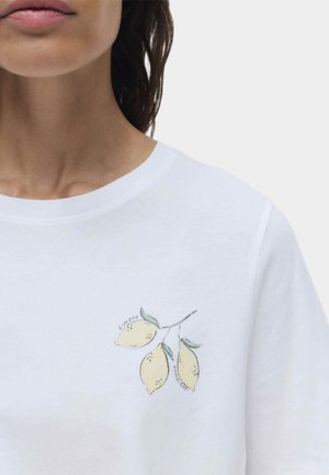 Primo piano di una persona che indossa una camicia bianca con un'illustrazione di un piccolo ramo di limone e il testo "Limone" e "Costiera Amalfitana" sul petto.