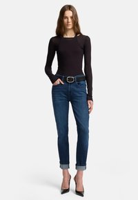 Camicia nera a maniche lunghe con un design aderente; jeans in denim blu con orli arrotolati; cintura nera con una grande fibbia argentata; scarpe nere con tacco alto.