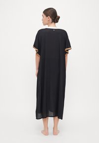 Črn, ohlapen kaftan s kratkimi rokavi. Zlata obroba okrog rokavov in okrogel ovratnik. Material se zdi lahek.