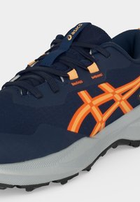 Μπλε ναυτικό αθλητικό παπούτσι ASICS με πορτοκαλί ρίγες, μαύρα κορδόνια, επενδεδυμένο γιακά και γκρι υφασμένο σόλα.