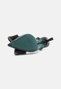 Black high-heeled shoe with a pointed toe and textured black fabric accents. The sole is green with horizontal grooves.