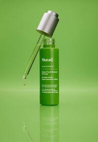 Grön glasflaska med Murad Retinol Youth Renewal Oil Drops, silver pipett, klar olja som droppar, vit text på flaskan. Reflekterande yta i bakgrunden.