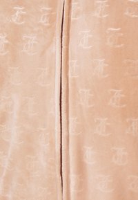 Ljusrosa, plyschig tyg med ett präglat mönster av sammanlänkade bokstäver. Slät textur med en subtil lyster, som framhäver en dragkedjestängning.