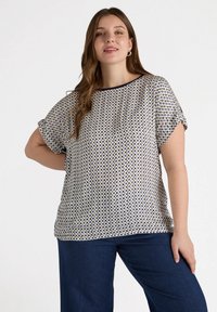 Kurzarmbluse in hellem Creme mit navyblauem geometrischen Muster, lockere Passform und rundem Halsausschnitt. Weicher Stoff mit glatter Textur.