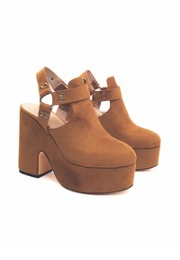 Scarpe con plateau in suede marrone, dotate di tacco largo, caratterizzate da cinturini incrociati con accessori in argento decorativi e design aperto sul retro.