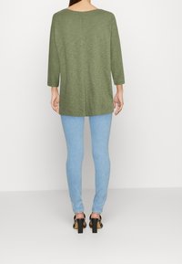 Olivgrüne, langärmlige Tunika mit lässiger Passform, kombiniert mit hellblauen Skinny Jeans und schwarzen Blockabsatzsandalen.