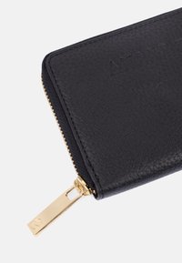 Portafoglio in pelle nera con superficie texture, hardware della cerniera dorato e logo incassato. Il tirante della cerniera è metallico e rettangolare.