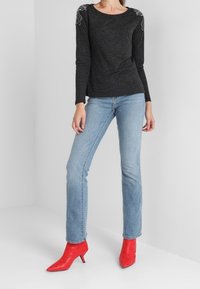 Un haut noir à manches longues avec des coutures décoratives sur les épaules, associé à un jean droit bleu clair et des bottines rouges à talons.