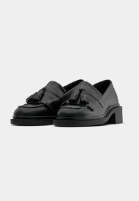 Mustat nahkakengät, joissa on lohkare korko, koristeelliset nauhat ja fringed yksityiskohtia edessä. Sujuva pinta ja minimalistinen muotoilu.