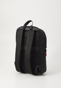 Črn nahrbtnik iz blaga s podloženo mrežasto hrbtno stranjo, nastavljivimi trakovi, ročajem za nošenje in rdečim zadrgo. Ima eleganten, minimalističen dizajn.