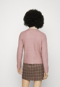 Stickad rosa tröja med en texturerad väv, rund halsringning och långa ärmar, i kombination med en rutmönstrad minikjol.