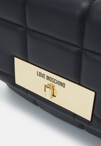 Borsa a tracolla in pelle trapuntata nera con una placca metallica dorata con la scritta "LOVE MOSCHINO" e chiusura a gancio. Superficie texturizzata e linee pulite.