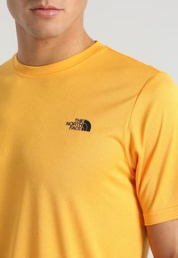 Kortärmad, rundhalsad t-shirt i en livlig gul färg. Har en svart logotyp på vänster bröst. Slät textur med en figurnära design.