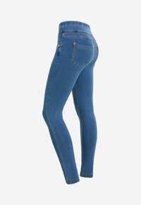 Jeans ajustados azules de talle alto con bolsillos traseros y costuras visibles, mostrados desde un ángulo lateral trasero sobre un fondo blanco.