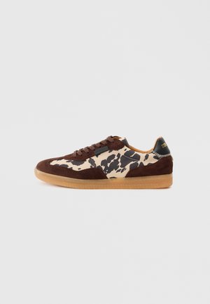 Sneakers maro din suede, cu un model de imprimeu cu vacă în tonuri de bej și negru, superior texturat și talpă din cauciuc, cu șireturi maro și un accent negru la călcâi.