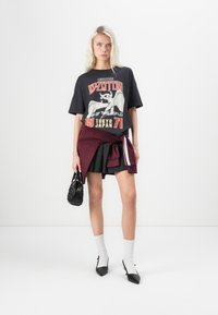 Black graphic t-shirt with Led Zeppelin design, oversized fit, paired with a dark skirt and burgundy wrap. Accessories include a small black handbag and white socks.