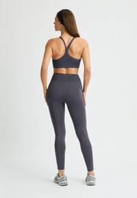 Grauer Sport-BH mit überkreuzten Trägern, kombiniert mit grauen High-Waist-Leggings. Glatte Textur mit passgenauem Design und Flachnaht.