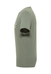 Zaļa īsām piedurknēm t-kreklu parādīts no sāna uz baltā fona, redzama labā piedurkne un daļa priekšējā teksta.