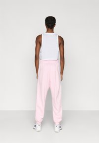 Balta bezroku topiņa kombinācija ar gaiši rozā sporta biksēm. Sporta biksēm ir elastīga jostasvieta un aproces, baltas sānu svītras, nēsātas kopā ar sporta apaviem.