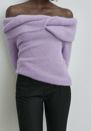 Pull tricot lavande épaules dénudées avec un détail plié sur la poitrine, associé à un pantalon noir ajusté.