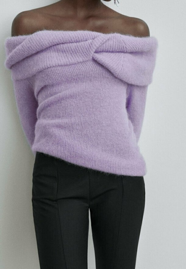 Pull tricot lavande épaules dénudées avec un détail plié sur la poitrine, associé à un pantalon noir ajusté.