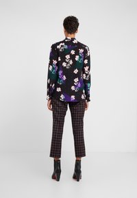 Zwarte blouse met bloemmotief en groene accenten, gecombineerd met geruite broek. Afgewerkt met glanzende zwarte laarzen met hak.