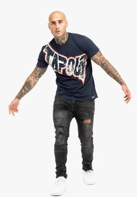 Jūrų pajėgų marškinėliai su dideliu nuniokotu "TAPOUT" grafiku balta ir raudona spalvomis. Sujungti su juodomis suplyšusiomis džinsais ir baltais sportbačiais.