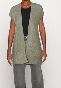 Cardigan a maglia verde oliva con maniche corte, apertura davanti e due tasche anteriori; realizzato in tessuto texturizzato con una vestibilità rilassata.