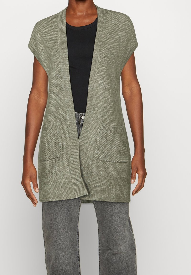 Cardigan a maglia verde oliva con maniche corte, apertura davanti e due tasche anteriori; realizzato in tessuto texturizzato con una vestibilità rilassata.