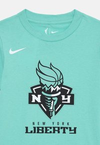 T-shirt en coton vert menthe avec un logo noir et blanc des New York Liberty, comprenant un design de torche et de basketball, à manches courtes et col rond.