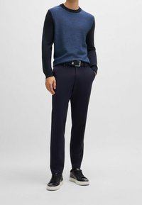 Blauer und schwarzer gestrickter Pullover mit strukturiertem Muster, kombiniert mit dunkelblauen Hosen und schwarzen Sneakers mit weißen Sohlen. Minimalistisches Design.